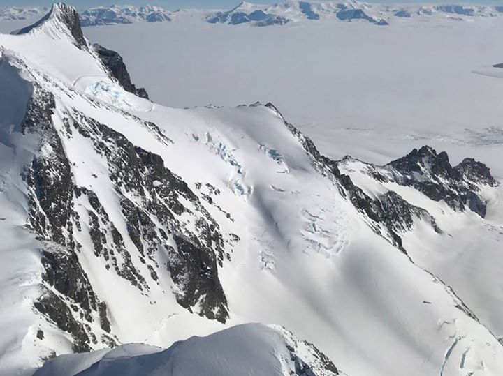 A spot of rocky, gray mountaintops are viewed peeking throug…